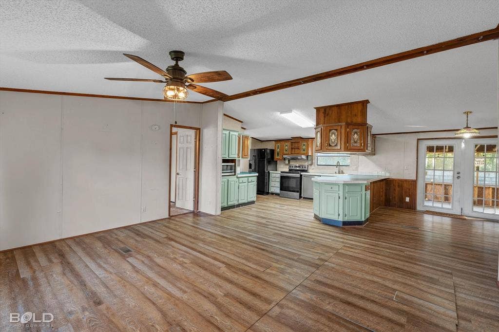 Open-concept interior featuring wood-finish flooring, a ceiling fan, and a kitchen equipped with a peninsula, light-toned cabinetry, and double glass-panel doors