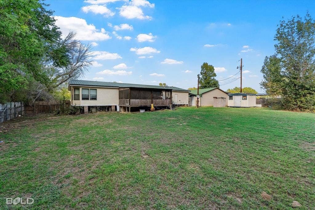 Expansive backyard featuring a large grass lawn, a metal-roofed structure, a screened-in wood porch, and a detached storage building