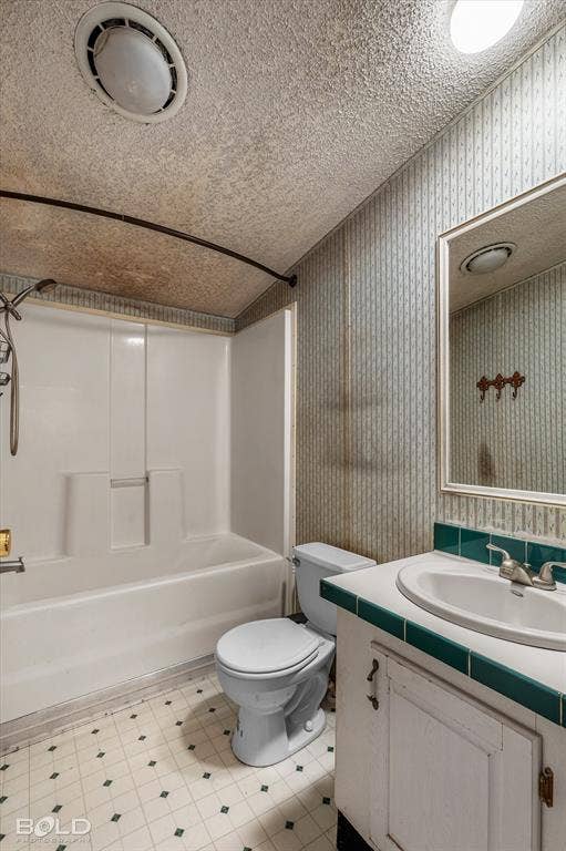 Bathroom featuring a molded composite tub and shower surround, vanity with tile countertop, integrated sink, and wall-mounted mirror