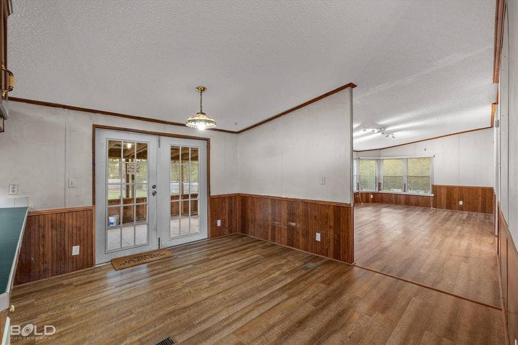Interior space featuring wood-finish flooring, wood wainscoting, glass-paneled double doors, and a decorative pendant light fixture
