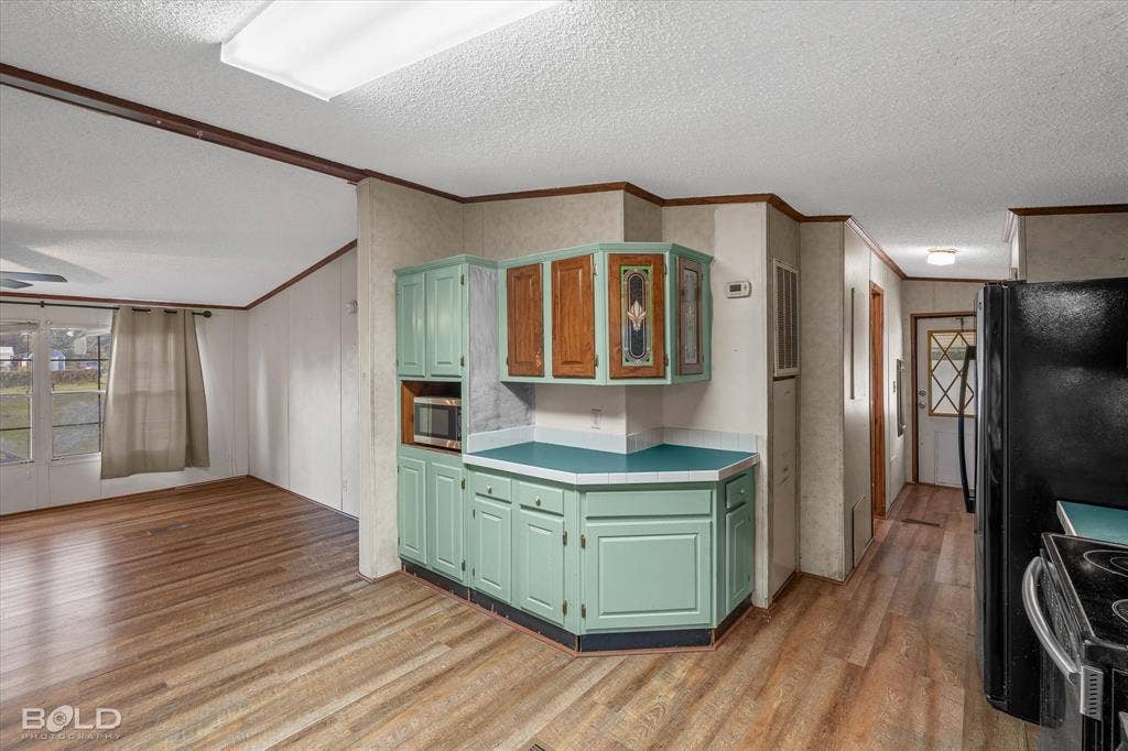 Kitchen featuring cabinetry with integrated stained glass detailing, tile-edged countertops, wood-finish flooring, and built-in microwave nook