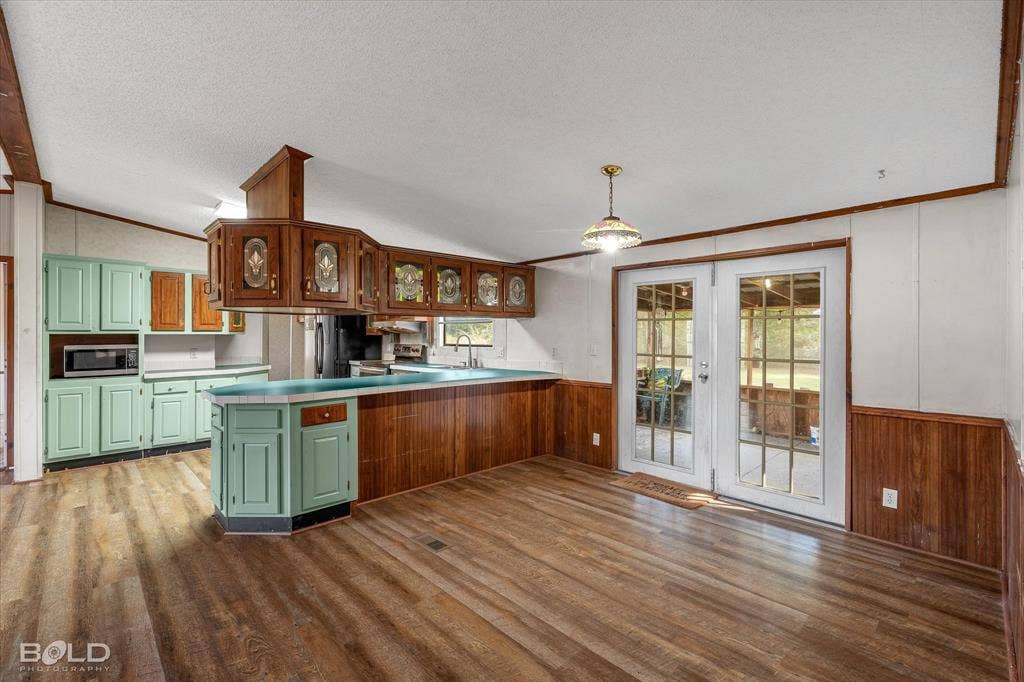 Kitchen area featuring wood-finish flooring, two-toned cabinetry, a peninsula breakfast bar, and glass-paneled double doors