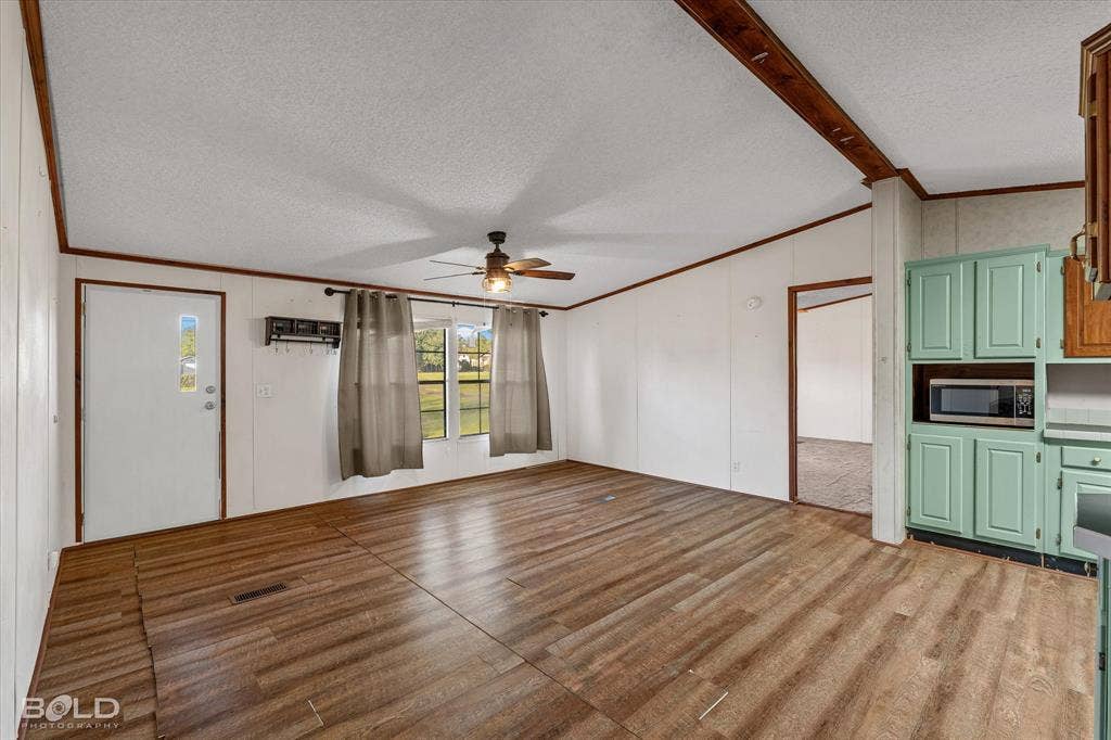 Open-concept living space featuring wood-finish flooring, exposed ceiling beams, a ceiling fan, and built-in cabinetry