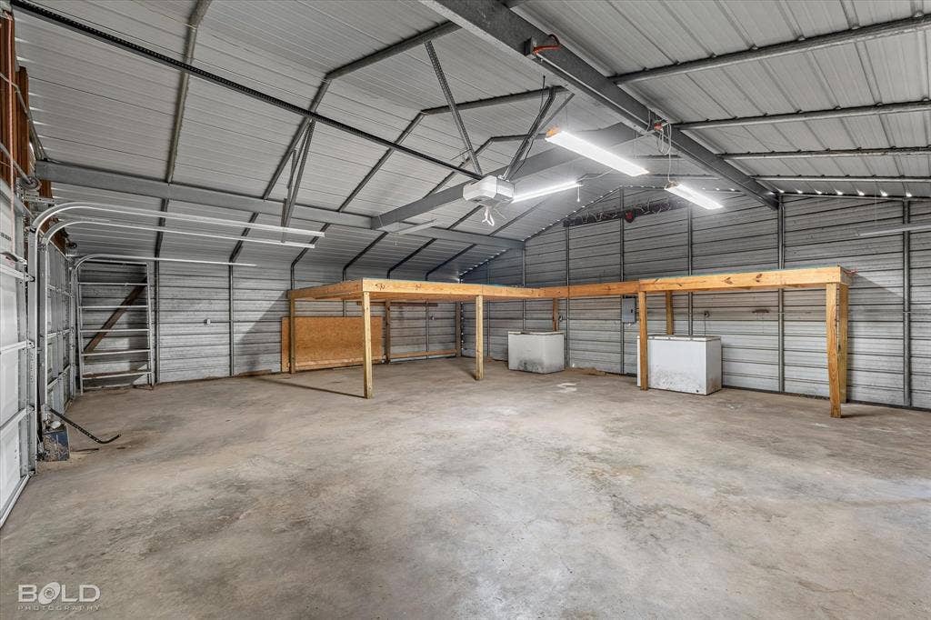Spacious detached garage featuring a concrete floor, metal-paneled walls and ceiling, exposed structural steel framing, and an elevated wooden mezzanine platform
