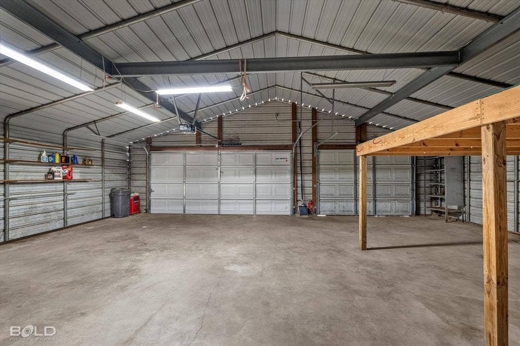 Expansive workshop featuring concrete flooring, steel structural framing, metal paneled walls and ceiling, dual overhead garage doors, and built-in wall shelving