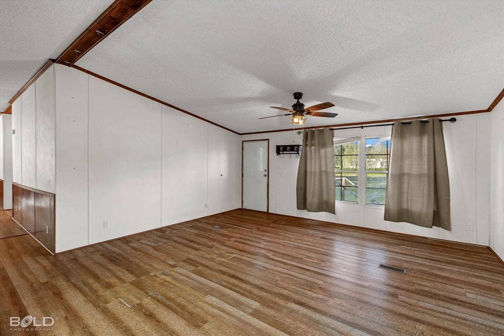 Wood-finish flooring, white paneled walls, wood-trimmed ceiling beams, and a ceiling fan with integrated lighting