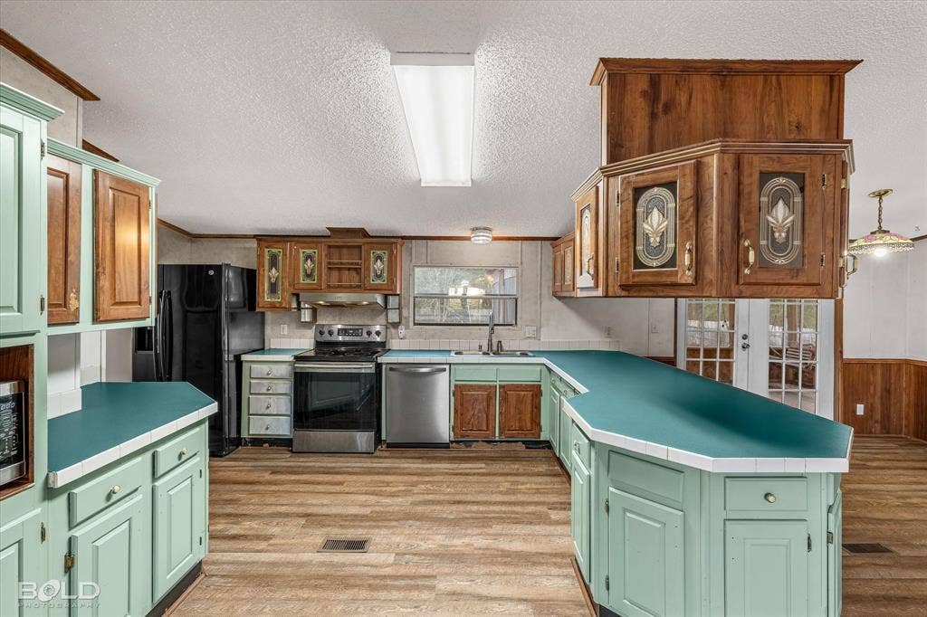 Kitchen featuring wood-finish flooring, solid-surface countertops, custom two-tone cabinetry with glass-panel inserts, stainless steel appliances, and French doors