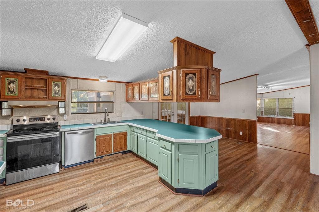 Kitchen featuring a peninsula, stainless steel dishwasher, stainless steel range, wood-finish flooring, and solid wood cabinetry with decorative glass inserts