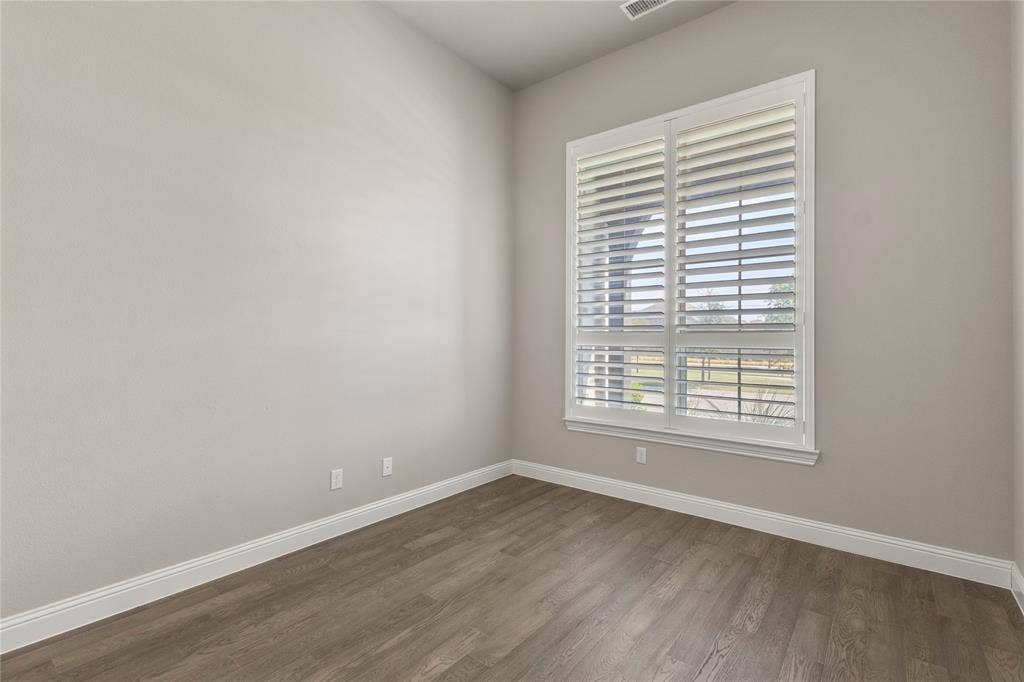 Neutral-toned interior featuring high ceilings, wood-finish flooring, and a large window with white plantation shutters