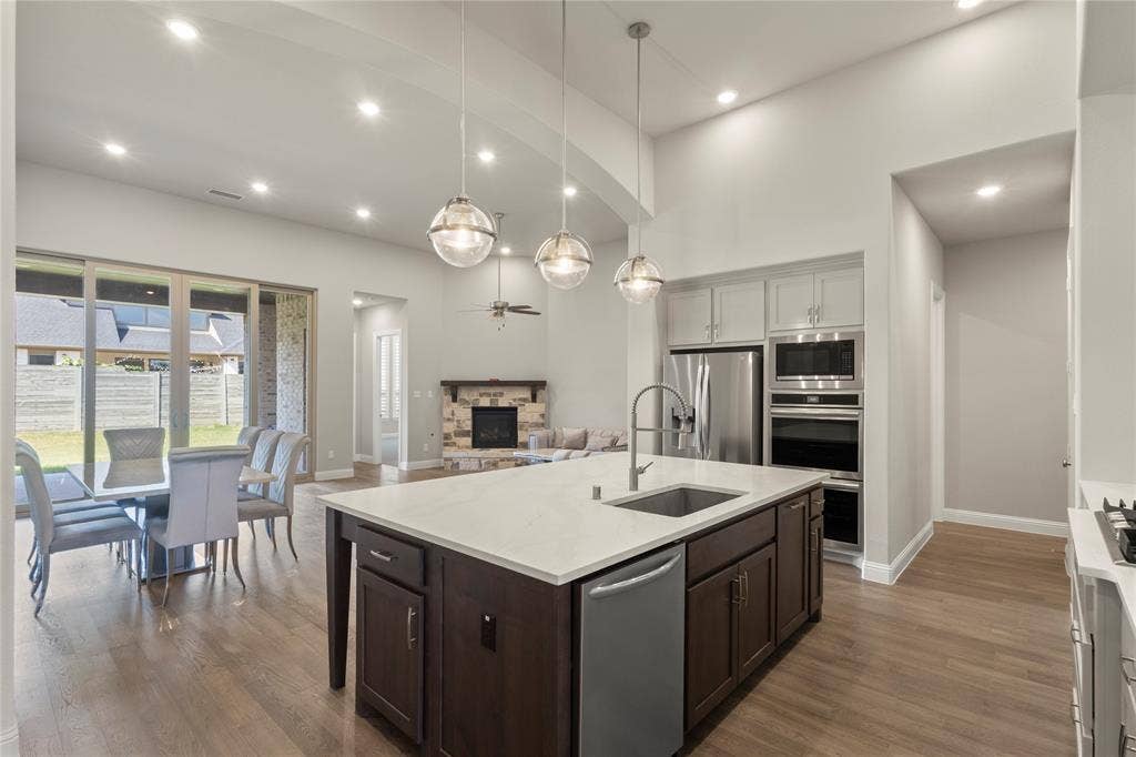 Open-concept kitchen featuring an island with a stone-finish countertop, stainless steel appliances, and wood-finish flooring