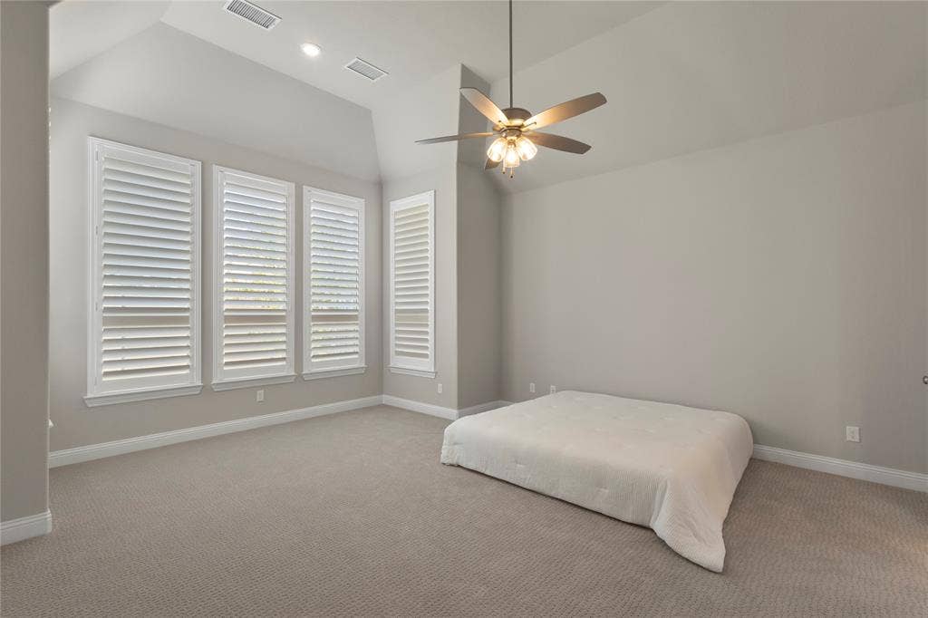 Vaulted ceilings, carpeted flooring, white plantation shutters, and a multi-light ceiling fan