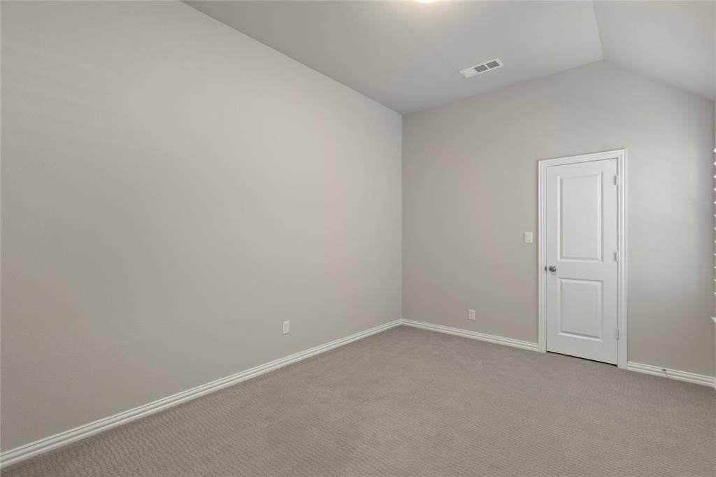 Neutral-toned interior space featuring vaulted ceilings, plush carpeting, and a two-panel interior door