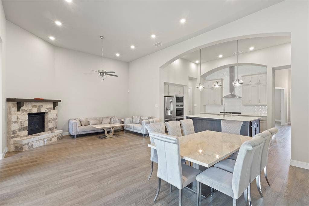 Open-concept interior featuring wood-finish flooring, a stone fireplace with a timber mantel, vaulted ceilings, a central kitchen island, and recessed lighting