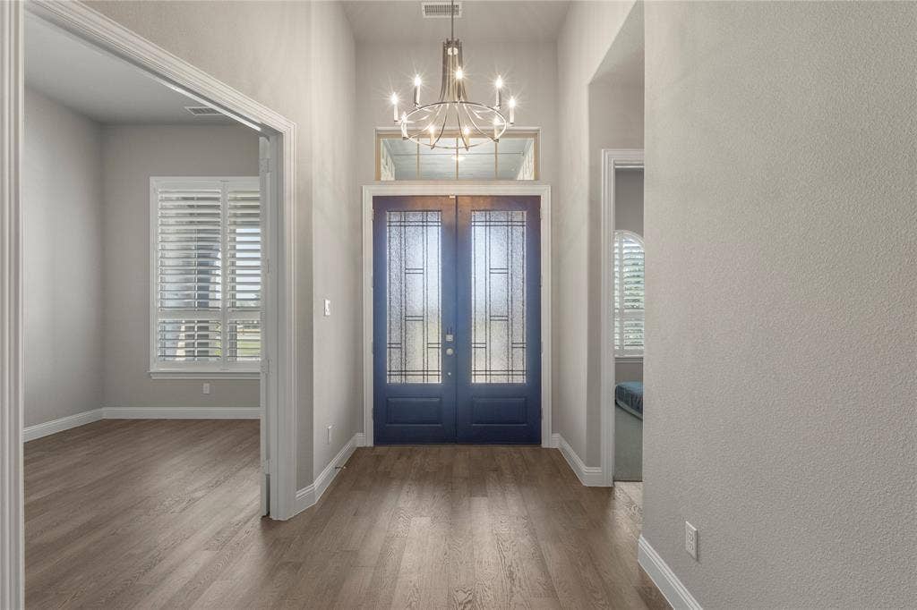 Foyer featuring double entry doors with decorative glass inserts, a transom window, wood-finish flooring, and a multi-arm chandelier