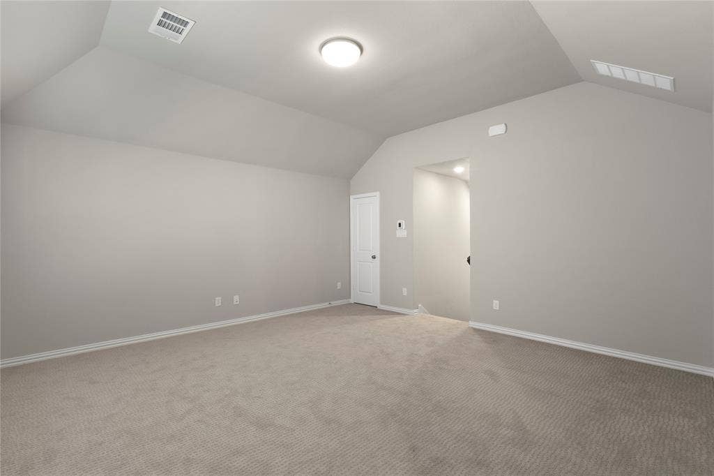Vaulted ceiling, neutral wall tones, and neutral-toned carpeting