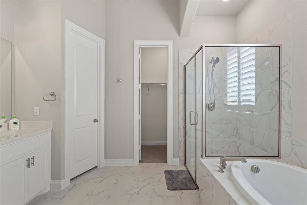 Bathroom featuring a white vanity cabinet, separate soaking tub, glass-enclosed shower with tiled surround, and large-format flooring