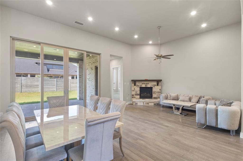 Open floor plan featuring wood-finish flooring, recessed lighting, corner stone fireplace with a wood mantel, and expansive sliding glass doors