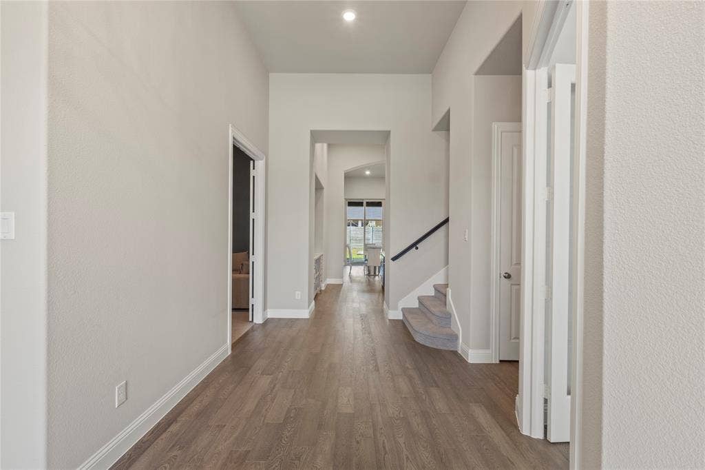 High-ceilinged entry featuring wood-finish flooring, recessed lighting, and a staircase with a dark metal handrail