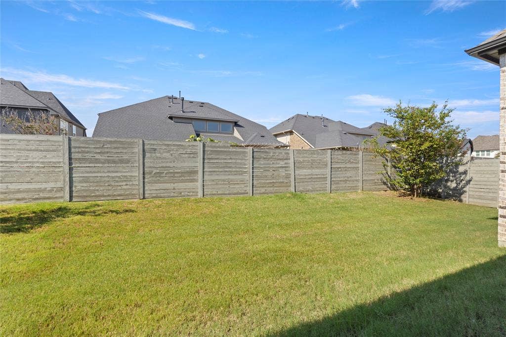 Backyard featuring a grass lawn, perimeter concrete fencing, and a mature tree