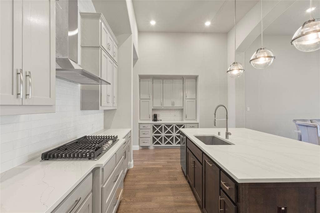 Kitchen featuring a large central island with quartz countertops, custom cabinetry, built-in wine storage, stainless steel gas cooktop, and glass pendant lighting