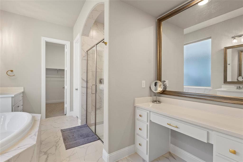 Bathroom featuring a soaking tub with stone-finish surround, walk-in shower with glass enclosure, dual vanity cabinetry with integrated seated station, and tile flooring
