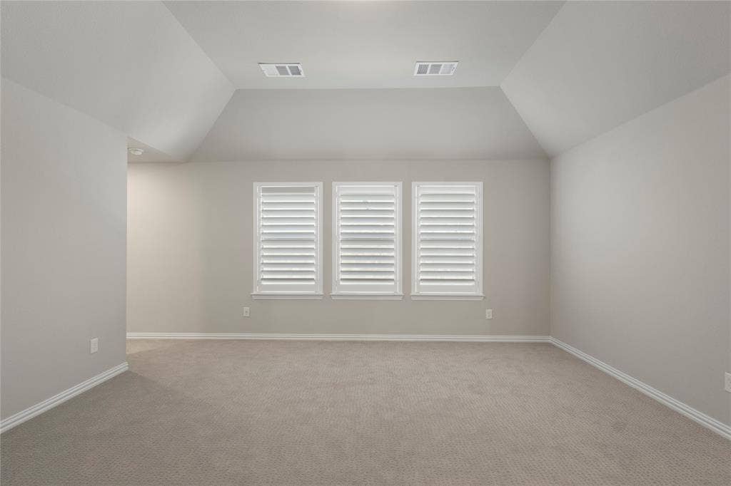 Vaulted ceiling, neutral wall tones, carpeted flooring, and three windows featuring interior shutters