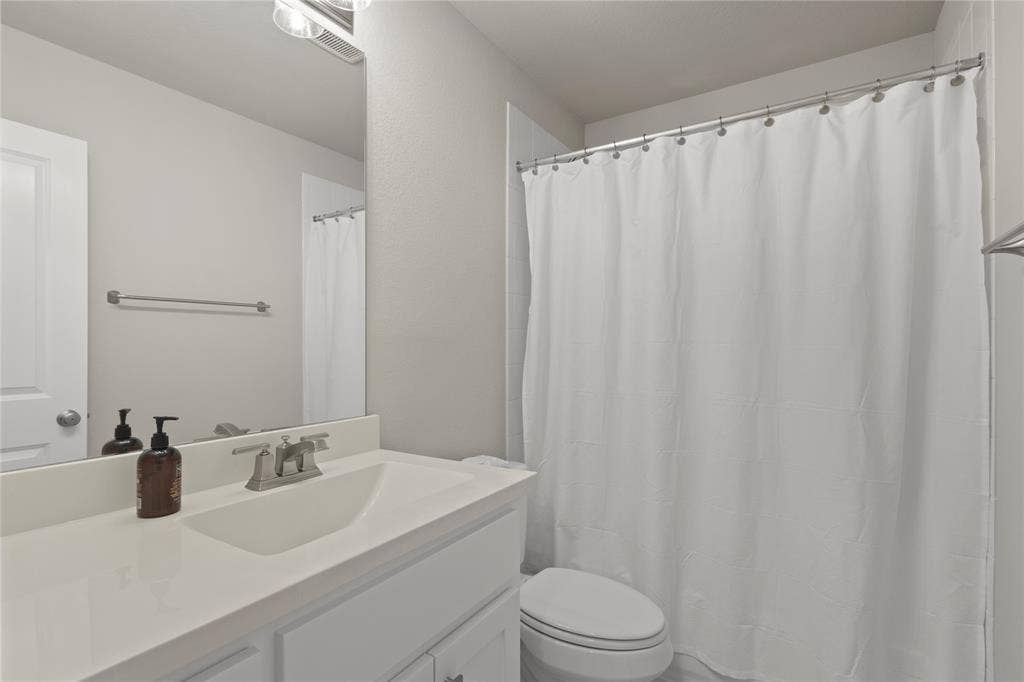 Bathroom featuring a white vanity with a solid-surface countertop, an integrated sink basin, a large wall-mounted mirror, and a tub-shower combination with a shower rod