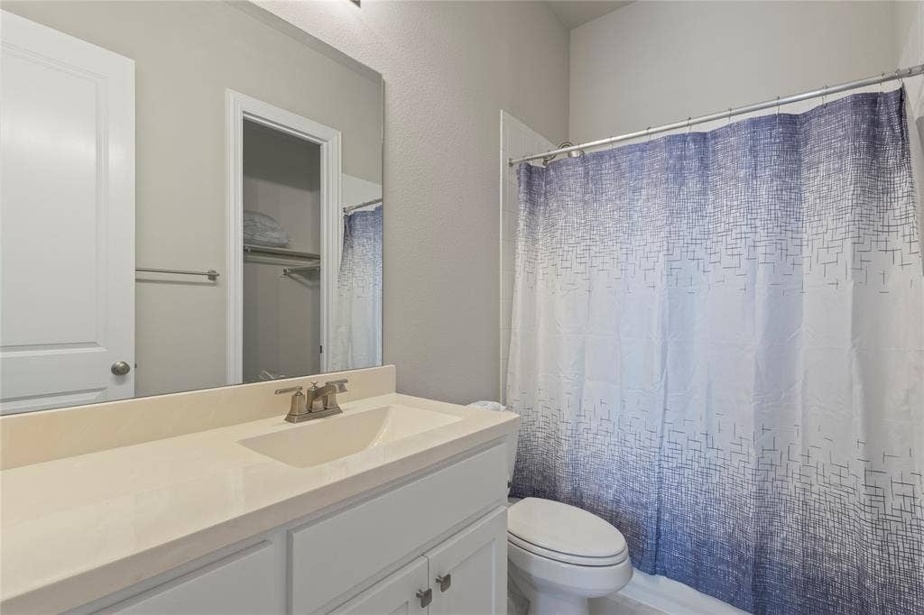 Bathroom vanity with a solid-surface countertop and integrated sink, chrome faucet, large wall-mounted mirror, and a tub-shower combination with a metal curtain rod