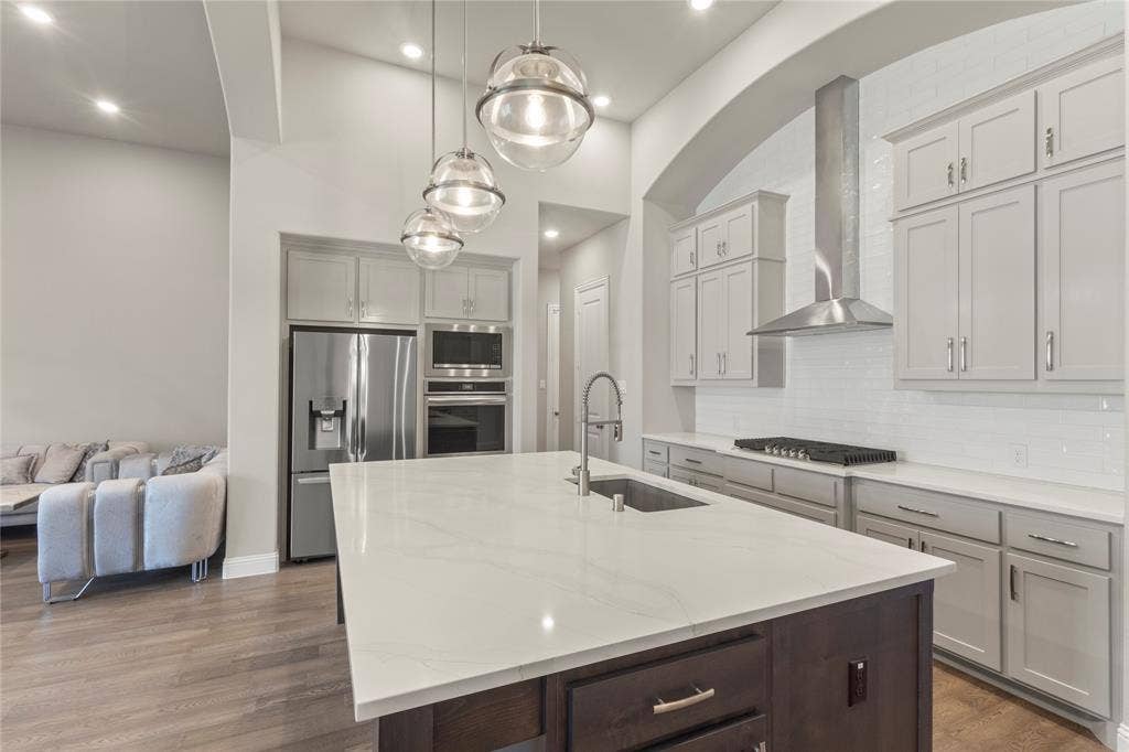 Kitchen featuring a quartz-topped center island with a stainless steel undermount sink, custom cabinetry, stainless steel appliances, and a tiled backsplash