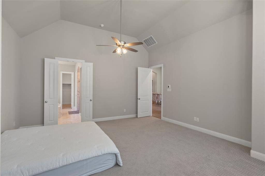 Vaulted ceiling featuring a central multi-blade ceiling fan with integrated light fixture, carpeted flooring, and neutral wall tones