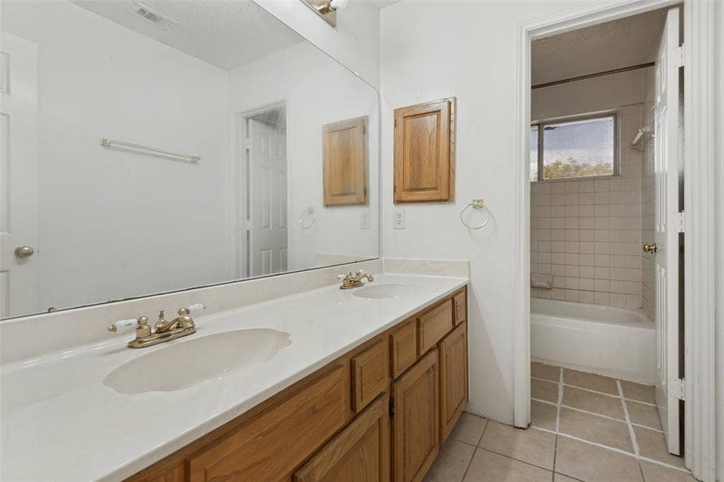 2306 Bent Brook Drive, Mesquite, TX 75181 Dual-sink vanity with a solid-surface countertop, full-width wall mirror, wood cabinetry, and a tile-surround bathtub