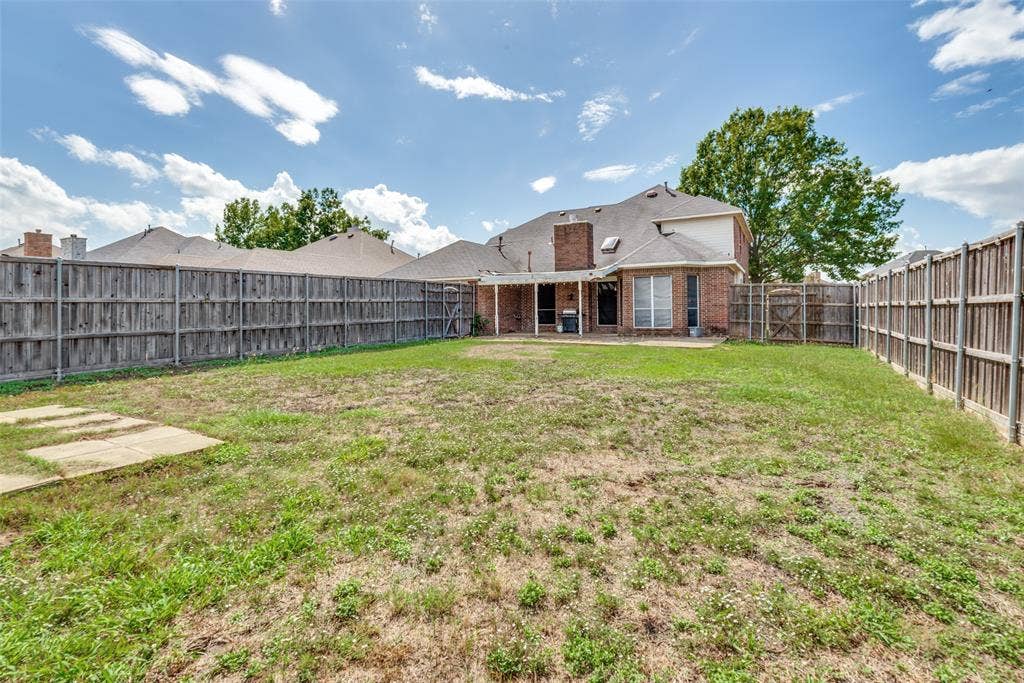 2306 Bent Brook Drive, Mesquite, TX 75181 Rear exterior featuring a brick facade, covered patio, masonry chimney, and full-height wood fencing