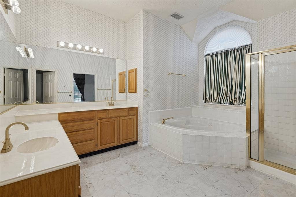 2306 Bent Brook Drive, Mesquite, TX 75181 Bathroom featuring a dual-sink vanity with light-toned countertops, a large jetted corner soaking tub with a tile surround, a glass-enclosed shower, and an arched window