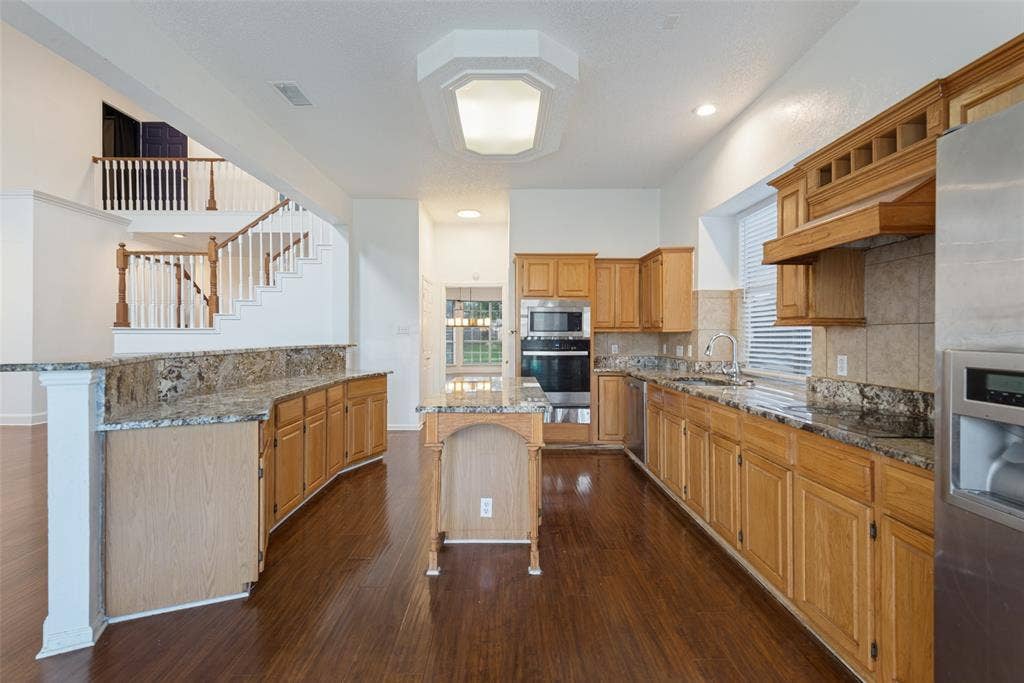 2306 Bent Brook Drive, Mesquite, TX 75181 Kitchen featuring wood cabinetry, stone countertops, a center island, stainless steel appliances, and dark wood-finish flooring