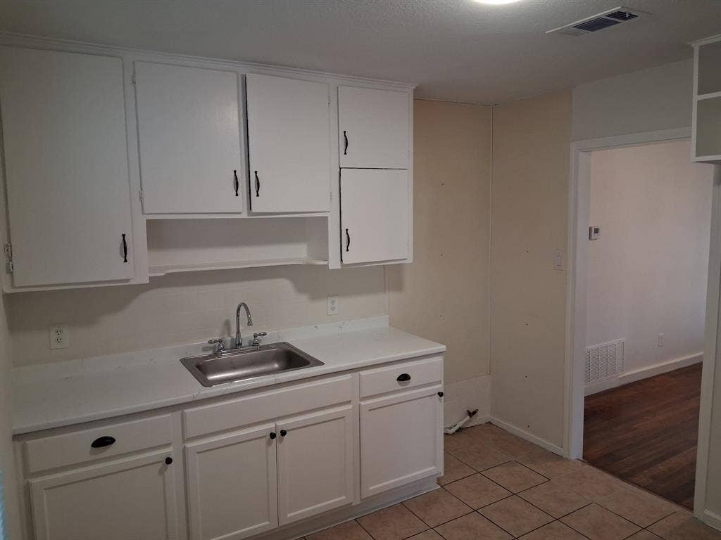 Kitchen featuring white cabinetry, integrated countertop, stainless steel sink with metal faucet, and tile flooring