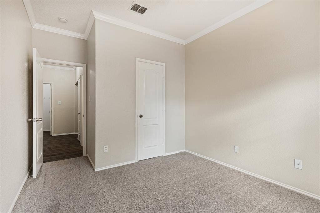 Neutral interior room featuring neutral wall paint, crown molding, a panel-style door, and wall-to-wall carpeting