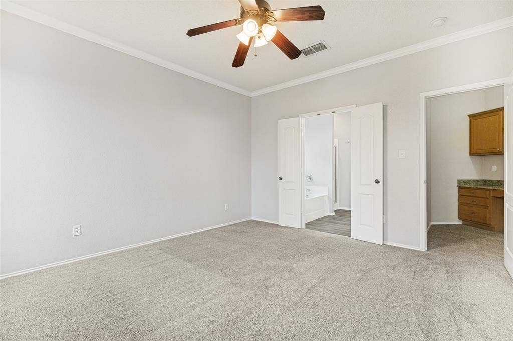 Neutral-toned interior featuring wall-to-wall carpeting, crown molding, and a multi-blade ceiling fan with integrated light fixture