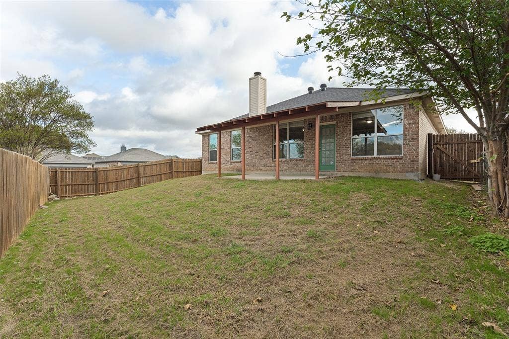 Brick exterior featuring a covered patio, exterior chimney, and fenced backyard