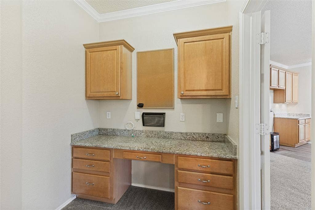 Built-in workspace featuring wood cabinetry, stone-surface countertop, and overhead storage units with crown molding