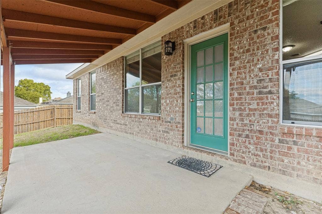 Covered concrete patio featuring a brick exterior, multi-pane glass door, and exterior wall-mounted lighting