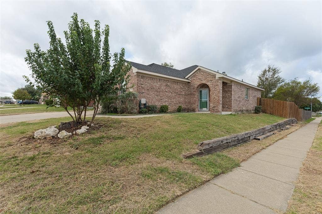 Single-story brick exterior featuring an arched entryway, stone landscaping accents, and timber retaining walls