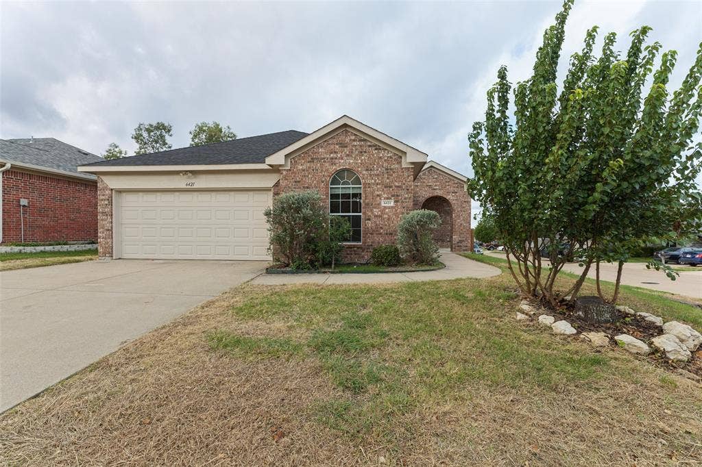 Brick exterior featuring a gabled roofline, an arched window, a two-car garage, and a concrete driveway