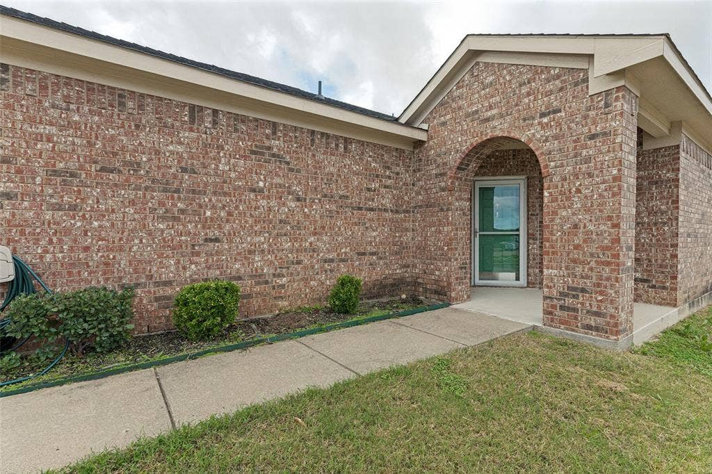 Brick exterior featuring an arched entryway, covered porch, and concrete walkway