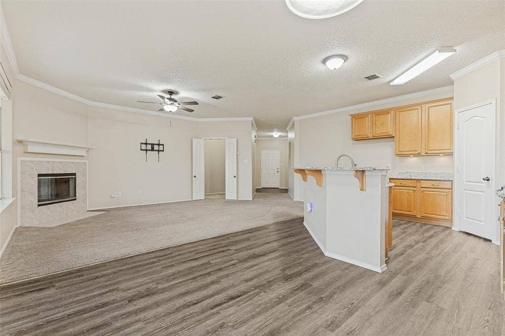 Open-concept interior featuring wood-finish flooring, a kitchen island with stone countertops, and a fireplace with a light-toned surround