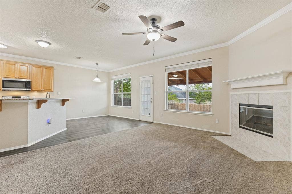 Open-concept space featuring wood-finish flooring, a fireplace with a light-colored tile surround and mantle, kitchen cabinetry with a breakfast bar, and a ceiling fan with integrated lighting
