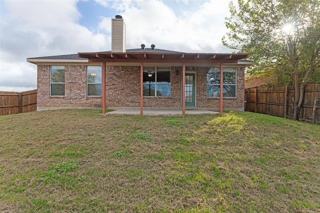 Brick exterior featuring a covered patio, concrete slab, chimney, and wood-style fencing