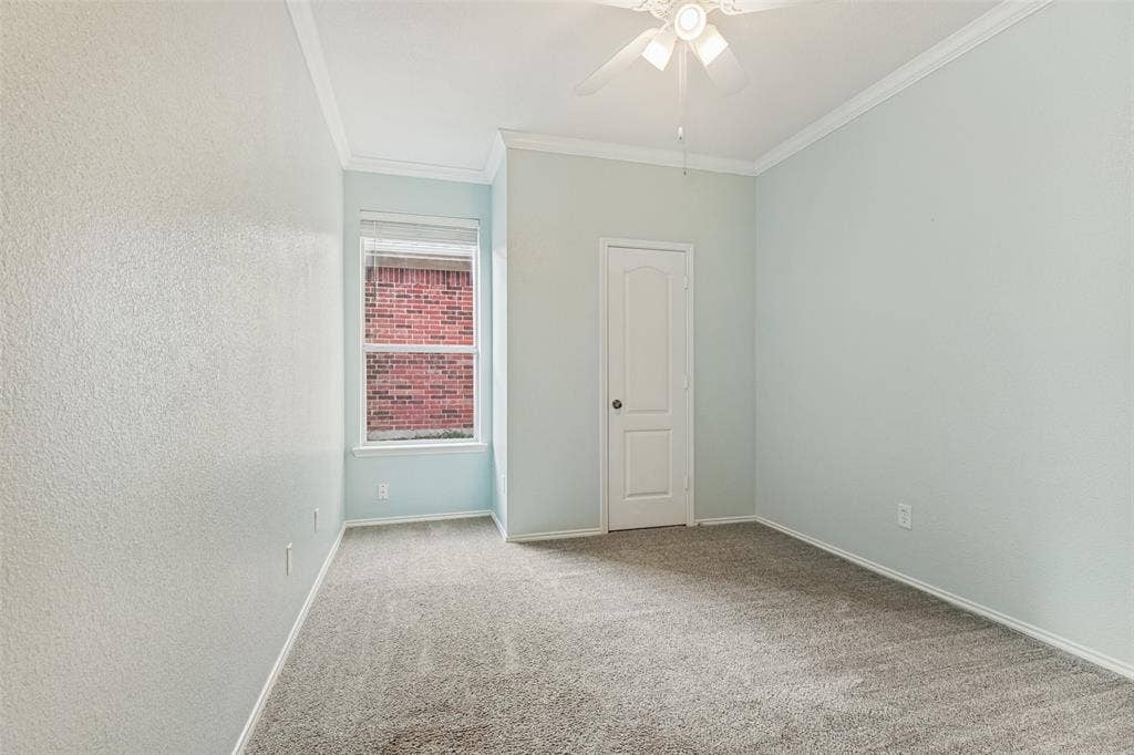 Interior room featuring neutral-toned carpeting, crown molding, a central ceiling fan with integrated lighting, and a single-panel interior door