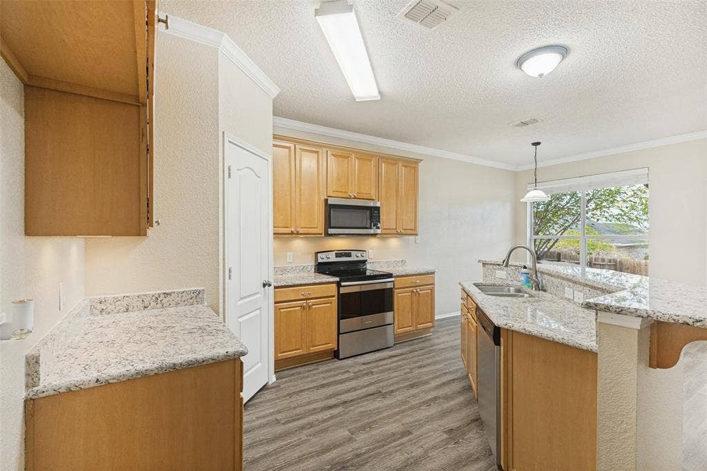 Kitchen featuring wood cabinetry, stone-finish countertops, stainless steel appliances, wood-finish flooring, and a breakfast bar