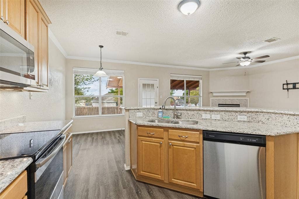 Kitchen featuring light wood cabinetry, stone-finish countertops, stainless steel appliances, wood-finish flooring, and a fireplace in the background