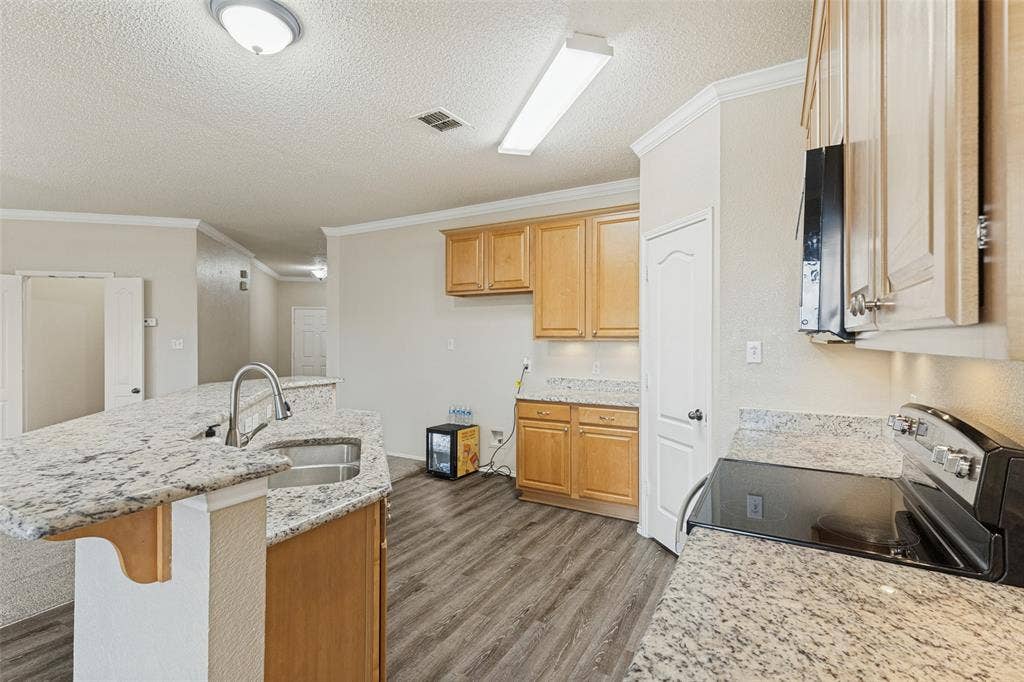 Kitchen featuring natural wood-finish cabinetry, stone-surface countertops, a double-basin stainless steel sink, and wood-finish flooring